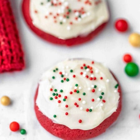 Two red velvet cookies next to colored sugar sprinkle balls.