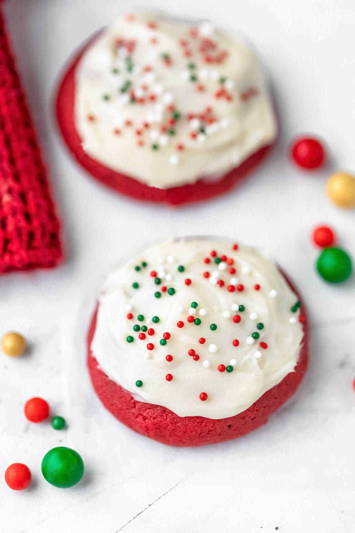 Two red velvet cookies next to colored sugar sprinkle balls.