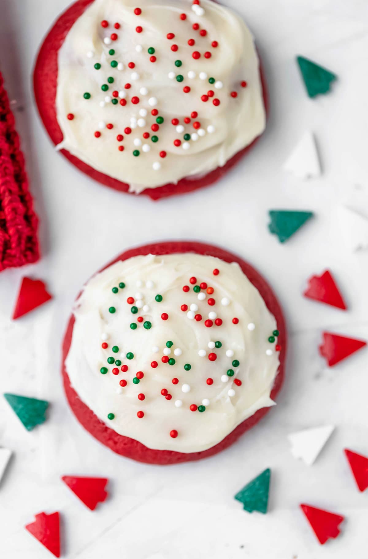 Two red velvet cookies surrounded by christmas tree sprinkles. 