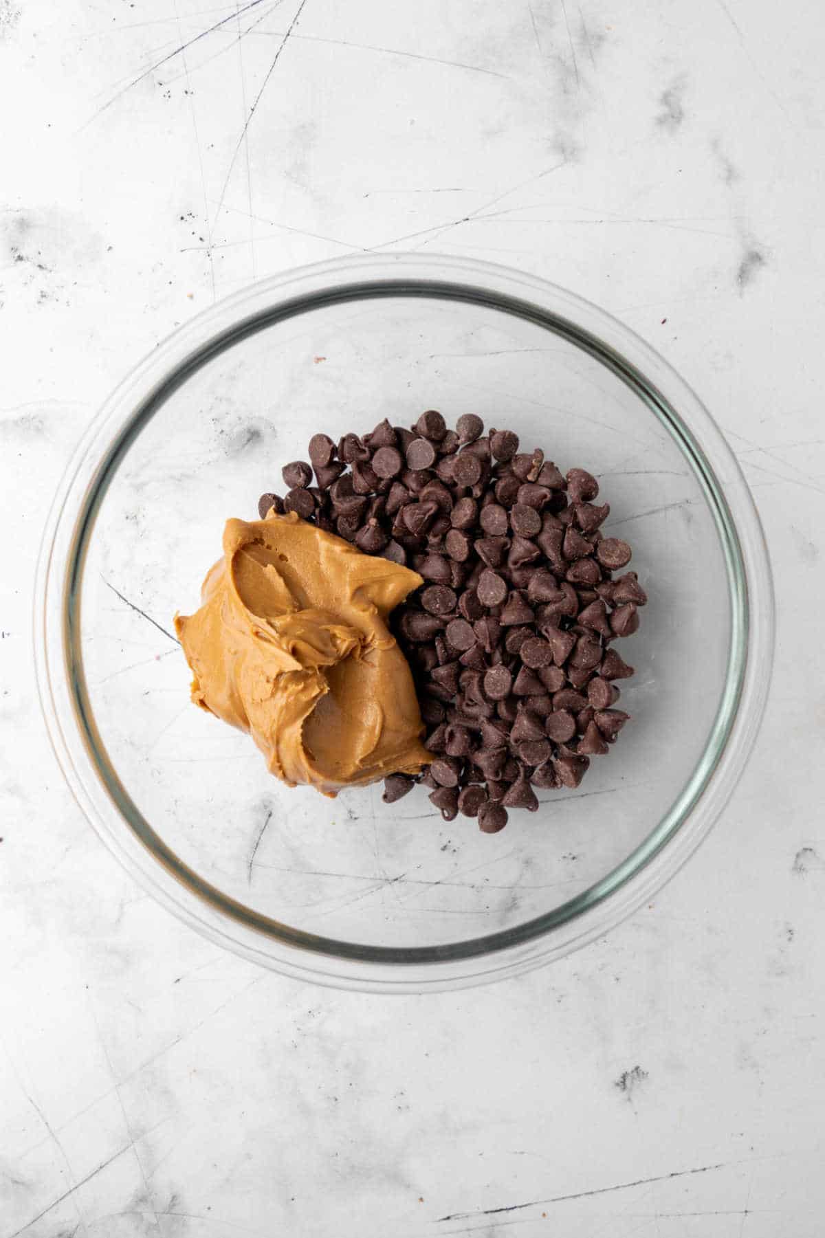 Peanut butter and chocolate chips in a glass mixing bowl. 