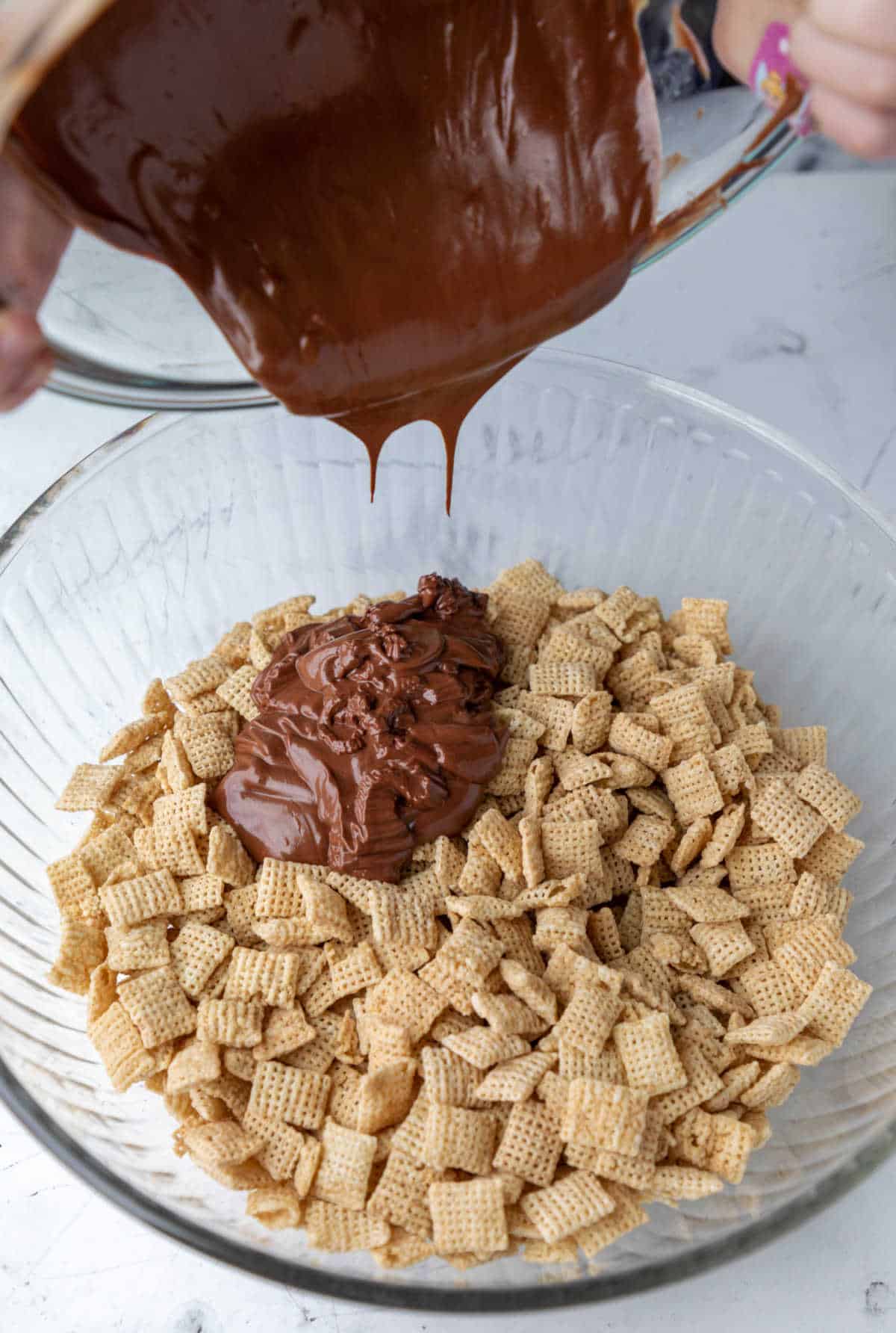 Peanut butter chocolate mixture pouring onto chex cereal. 