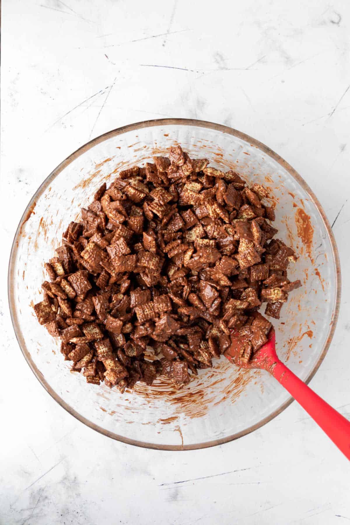 Spatula mixing peanut butter chocolate mixture into cereal. 
