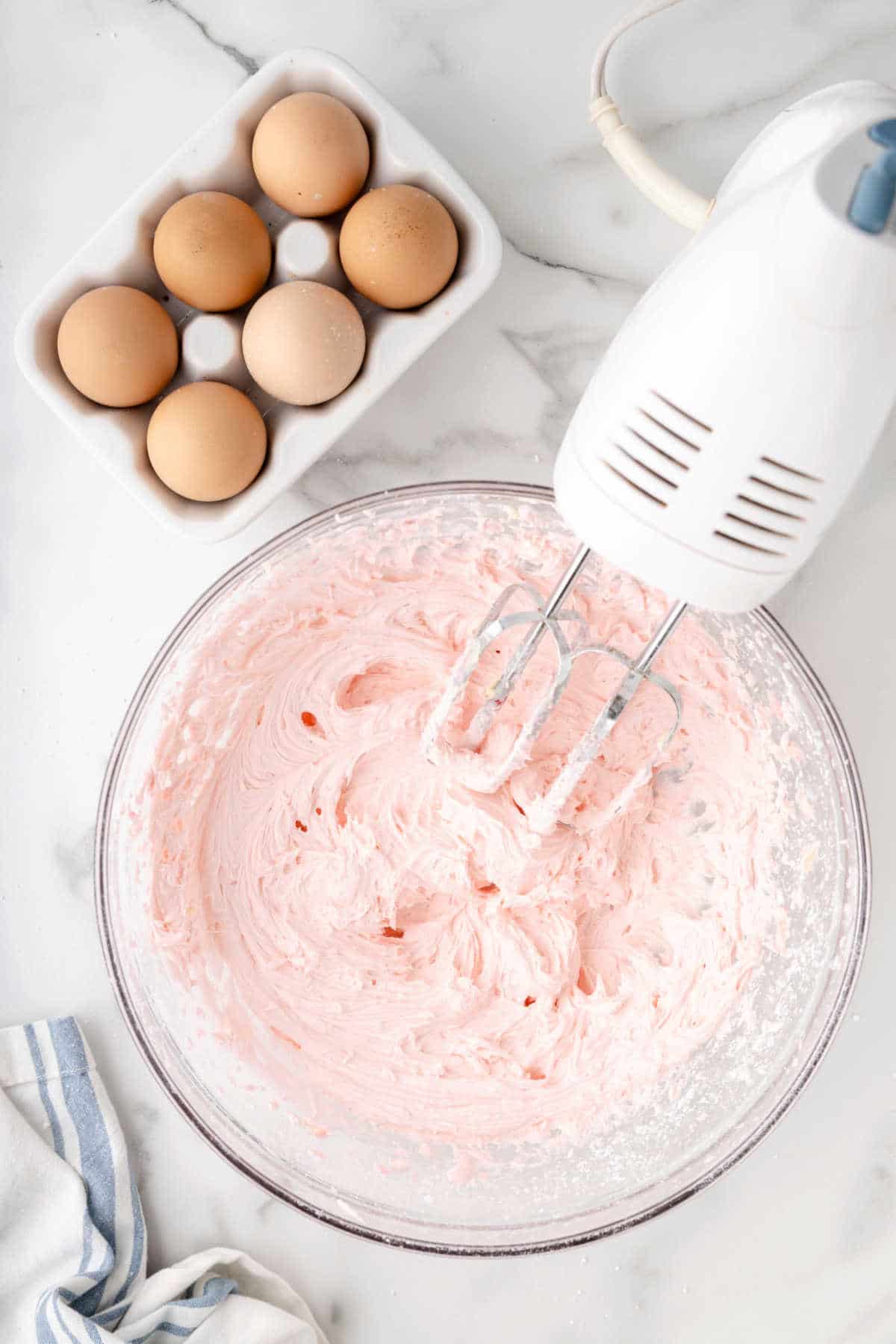 Pink buttercream frosting in a glass mixing bowl.