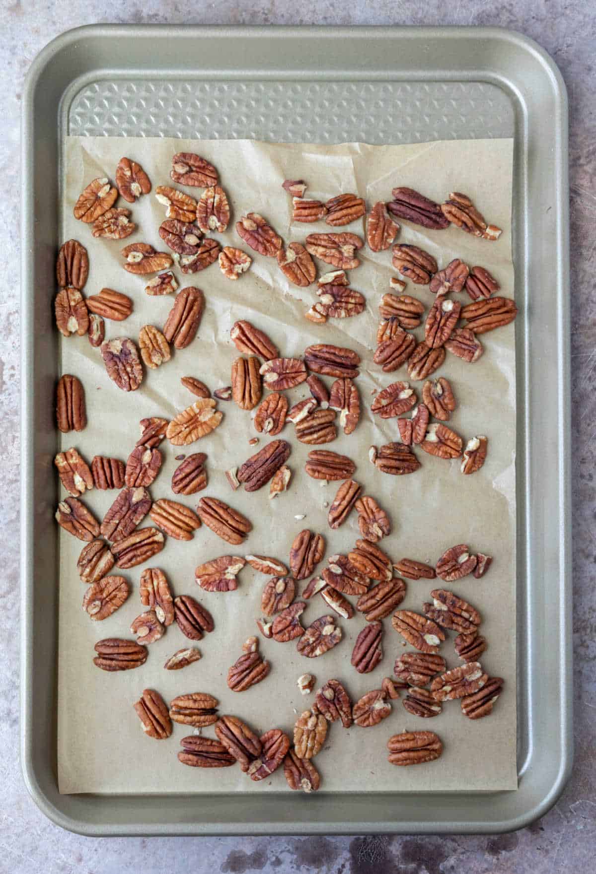 A rimmed baking sheet with a layer of pecans on it. 