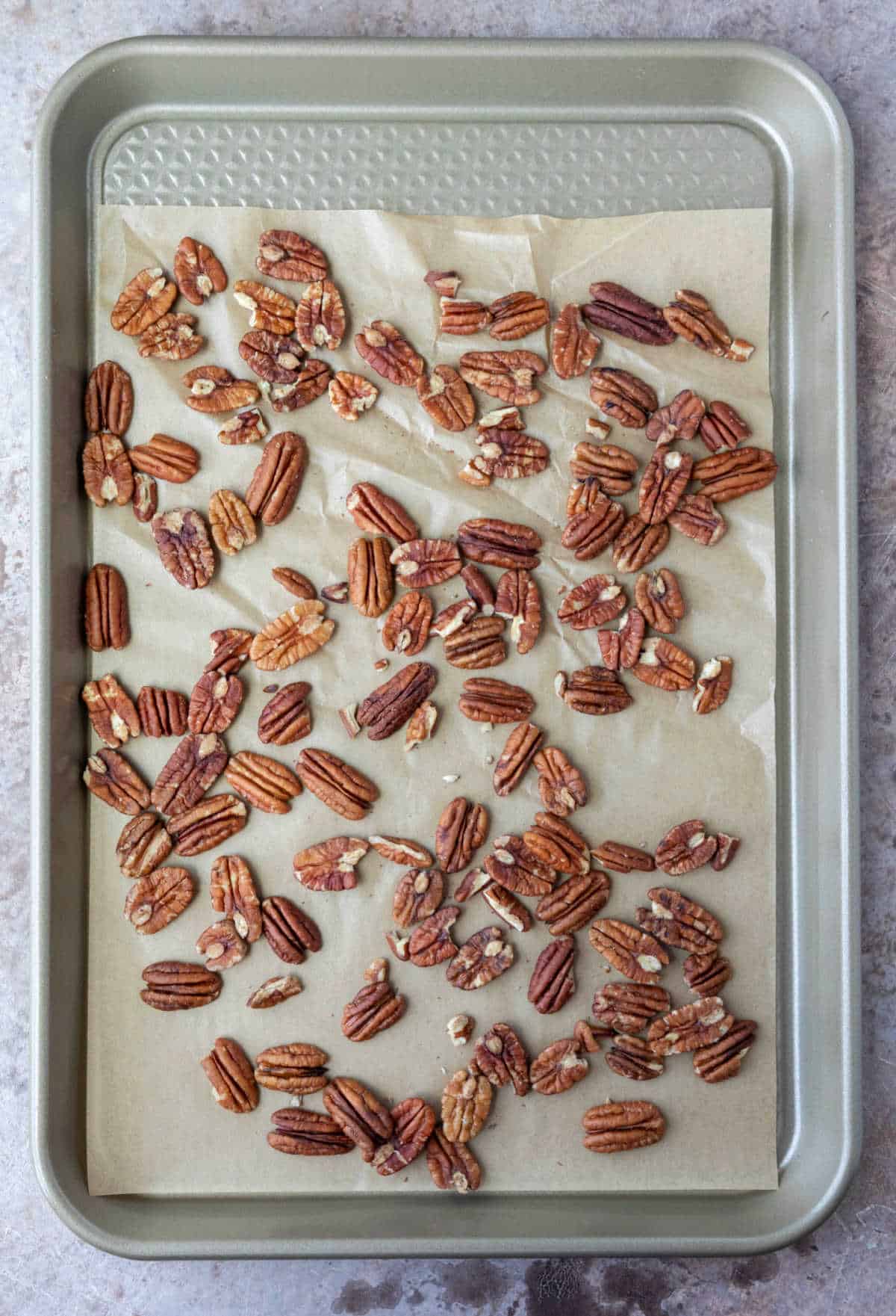 A rimmed baking sheet with a layer of pecans on it.