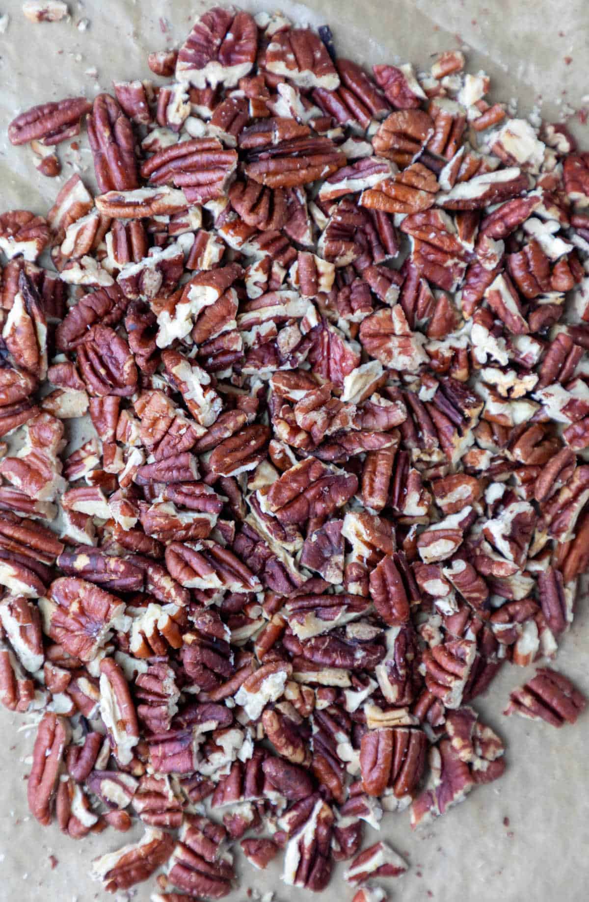 A pile of chopped pecans on a piece of brown parchment paper. 