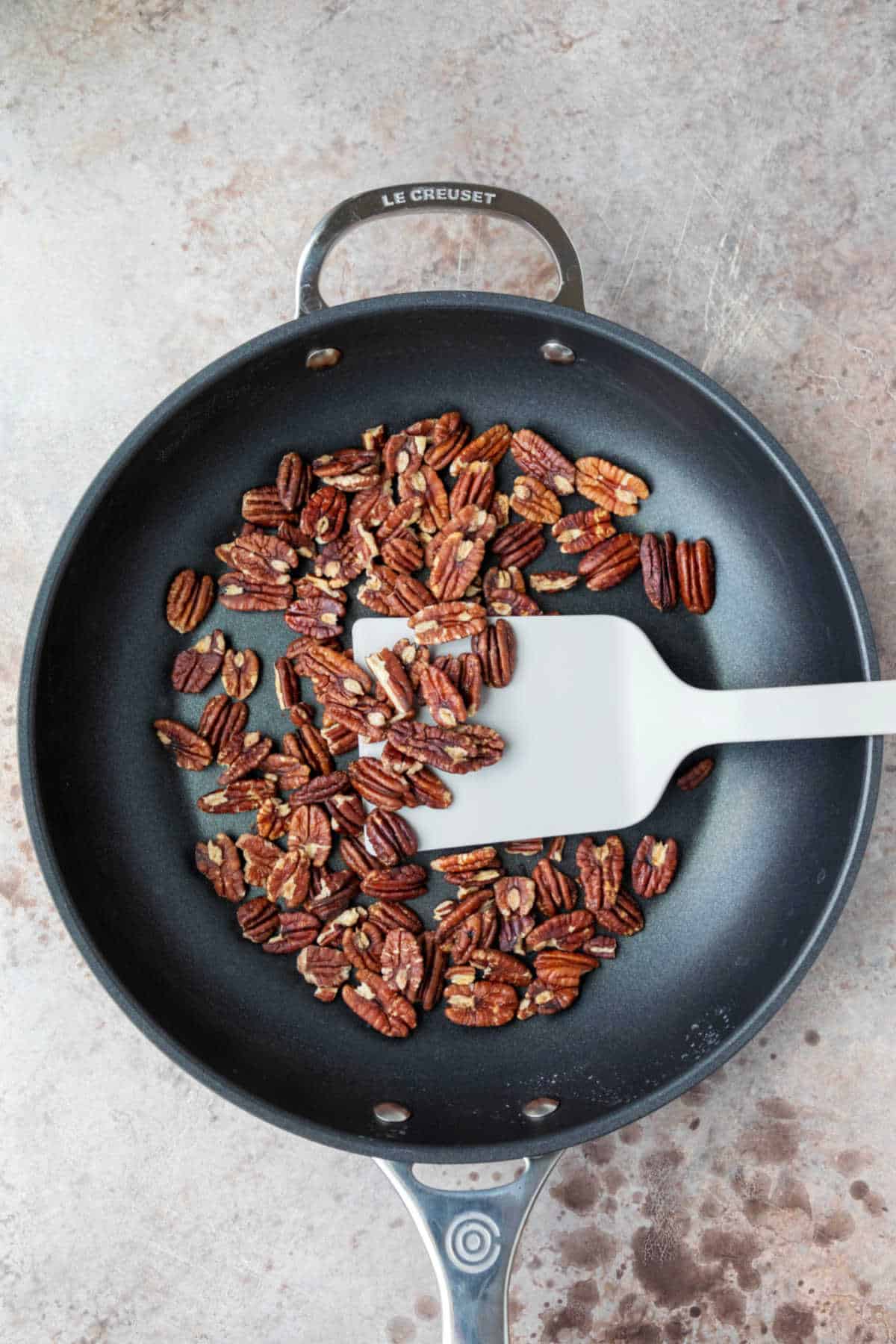 A spatula stirring pecans in a skillet. 