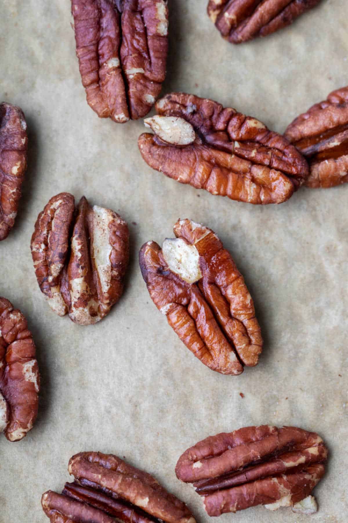 Close up photo of toasted pecans on a piece of brown parchment paper.