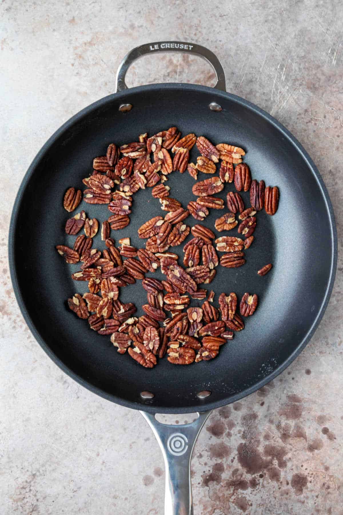 A skillet with a single layer of pecans in it.