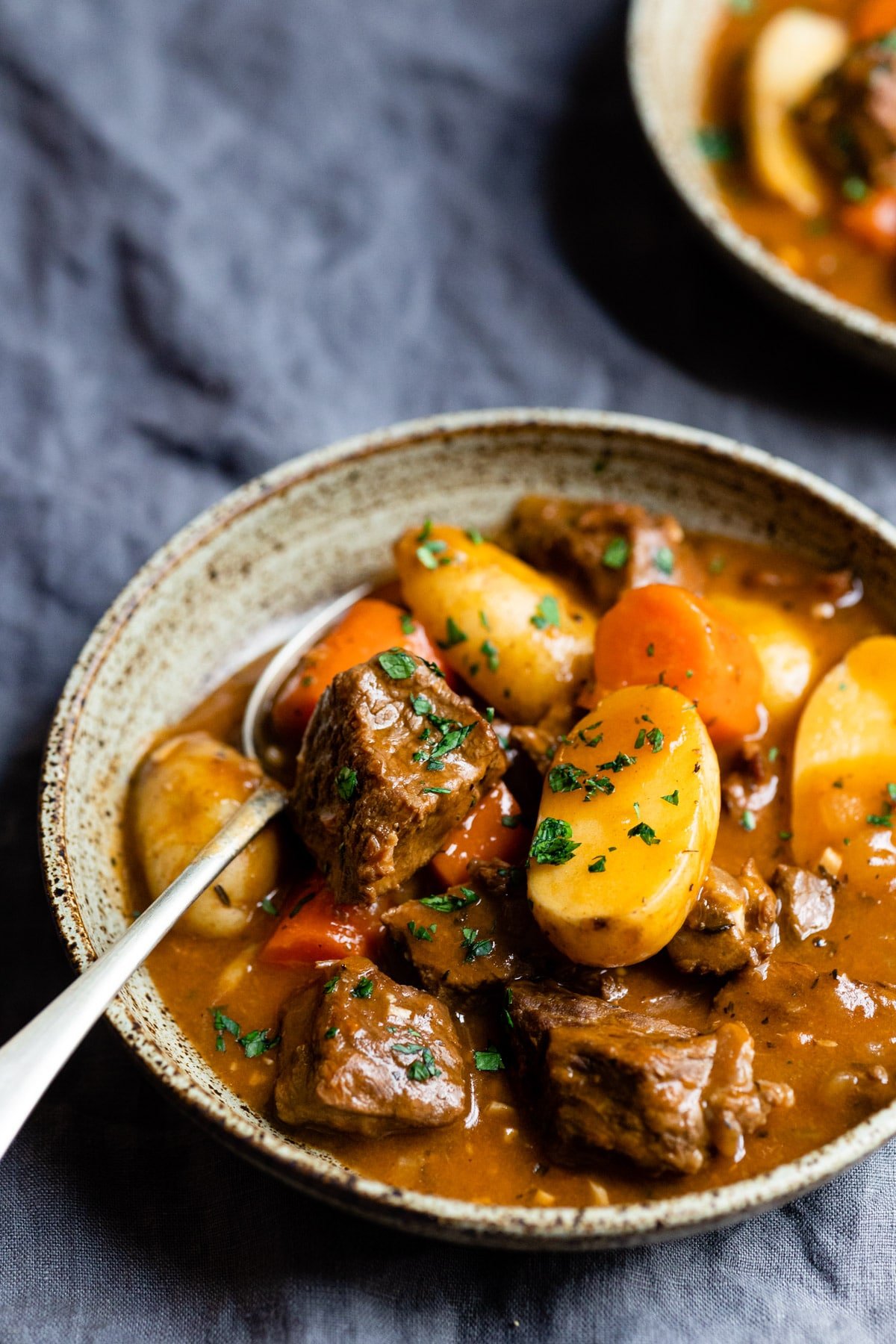 A silver spoon in a bowl of beef stew. 