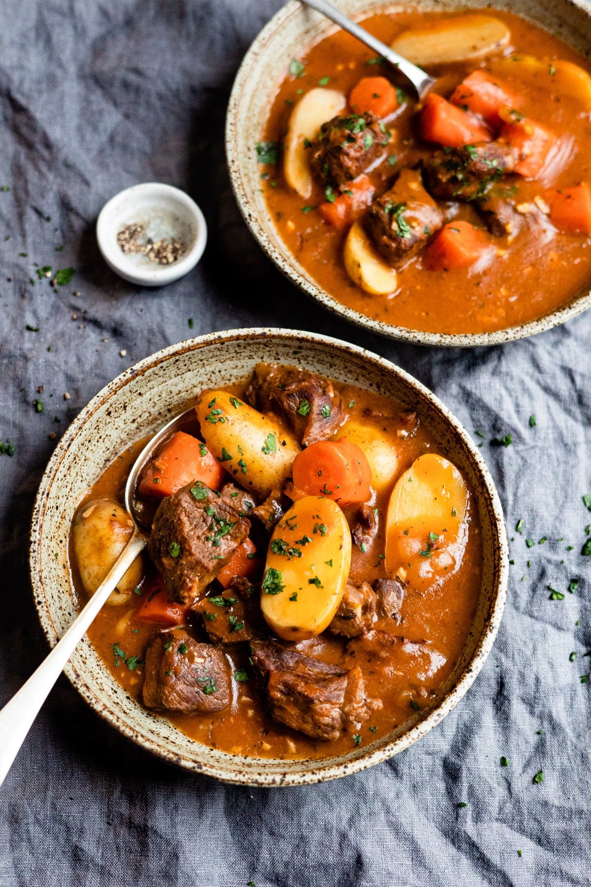 Two bowls of beef stew on a blue linen. 