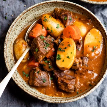 Bowl of beef stew topped with parsley.