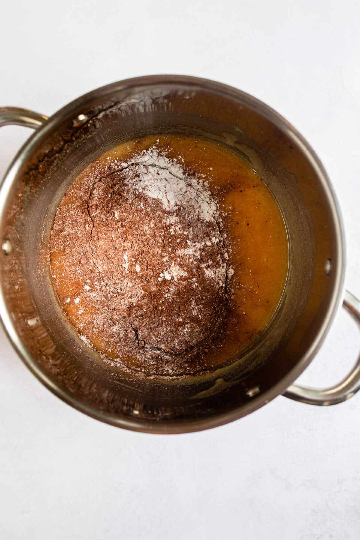 Dry ingredients on top of wet ingredients for brownies in a saucepan.