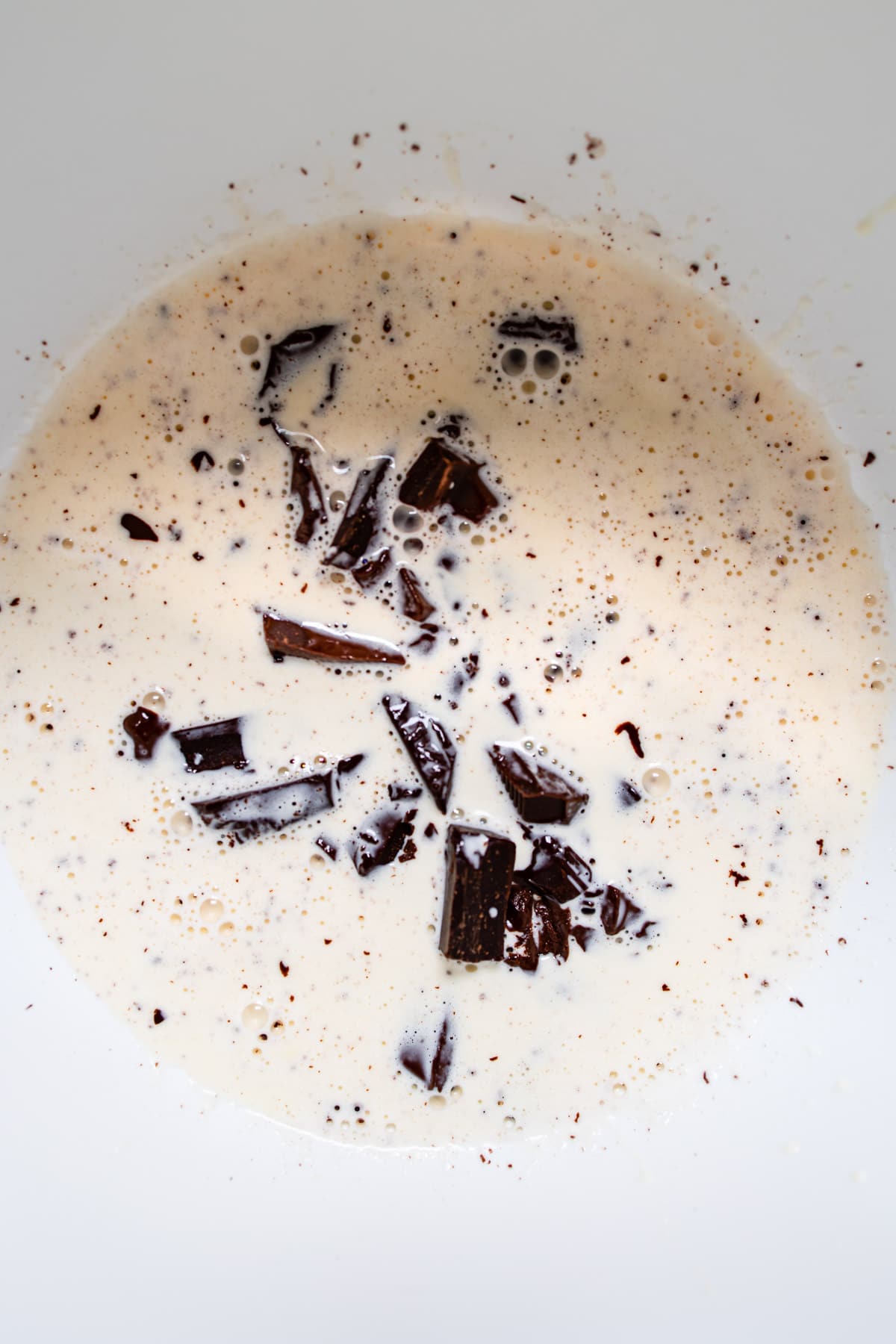 Chopped chocolate and cream in a white mixing bowl. 