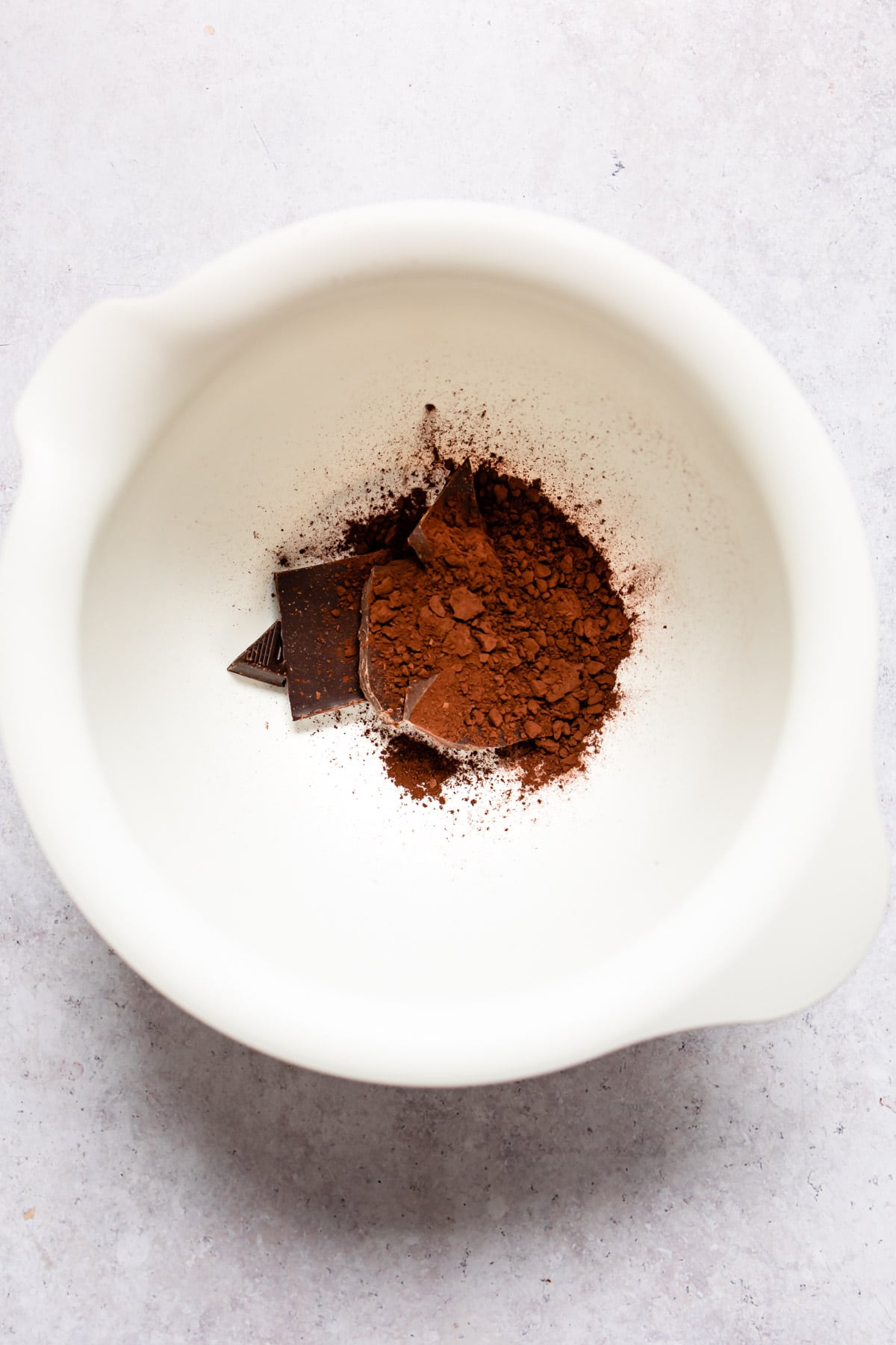 Chopped chocolate and cocoa powder in a white mixing bowl. 