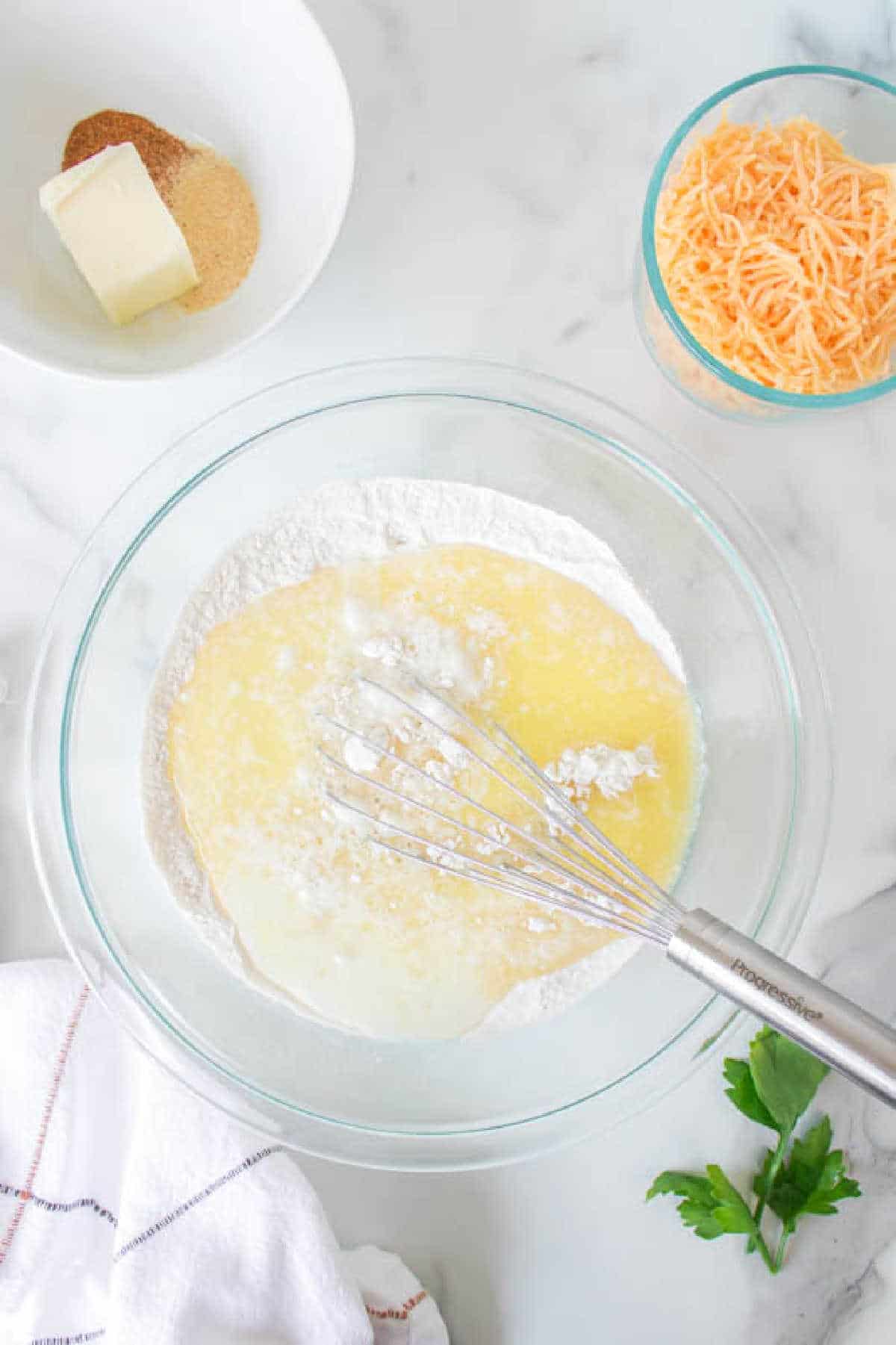 Buttermilk and melted butter whisked into dry ingredients in a glass mixing bowl.