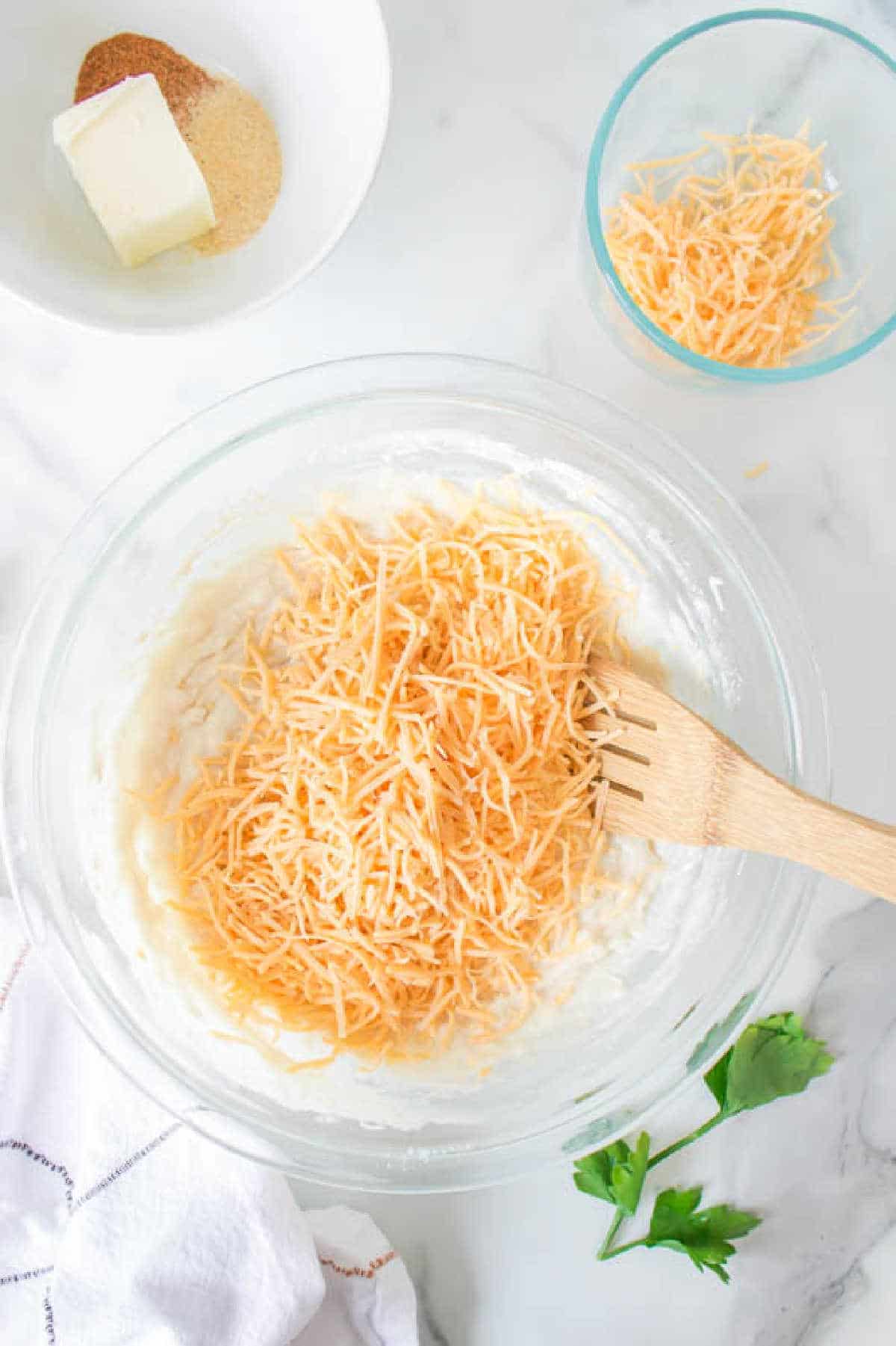 Shredded cheddar cheese on biscuit dough in a mixing bowl.