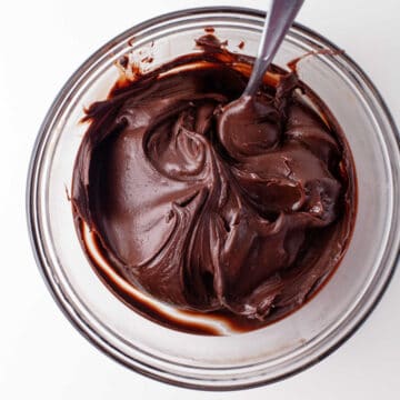 Chocolate ganache with a spoon in it in a glass mixing bowl.
