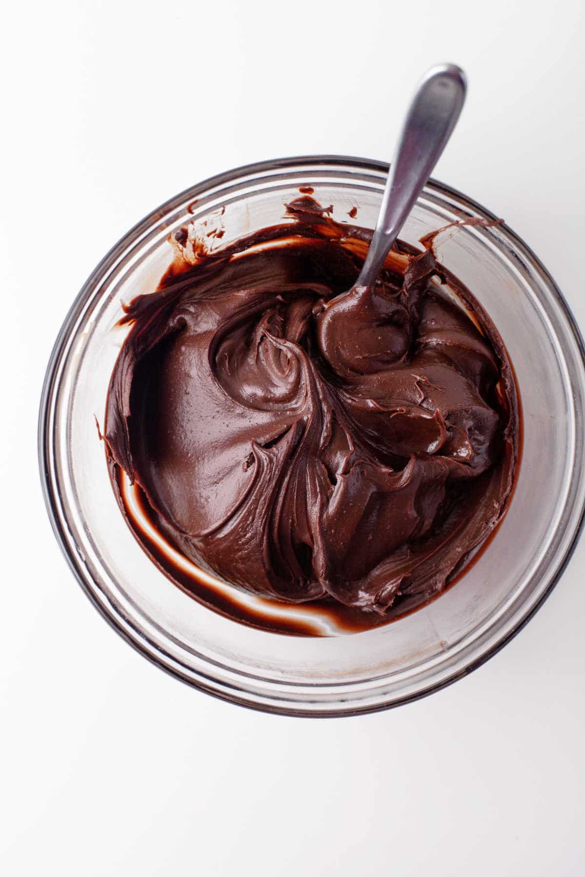 Chocolate ganache with a spoon in it in a glass mixing bowl.