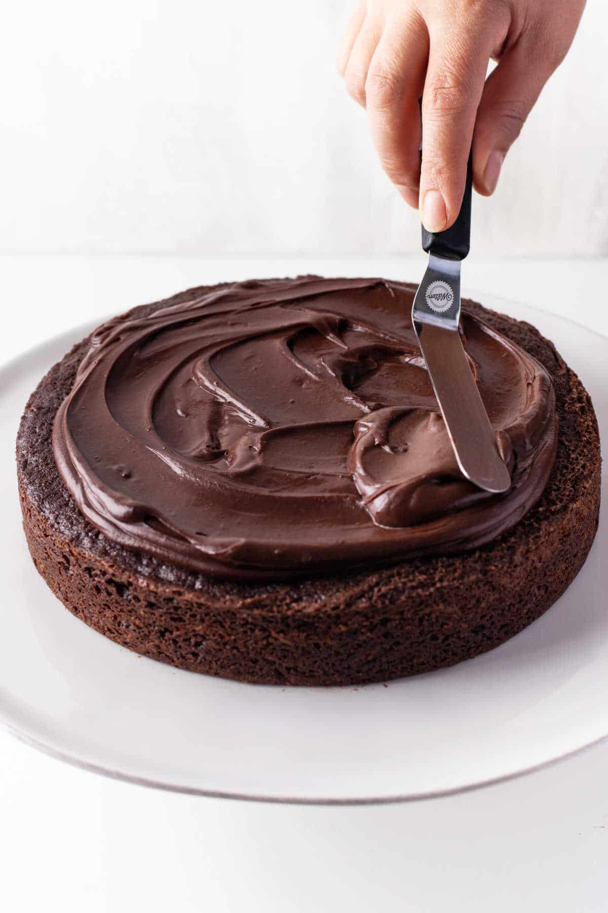 An offset spatula spreading chocolate ganache on a chocolate cake. 