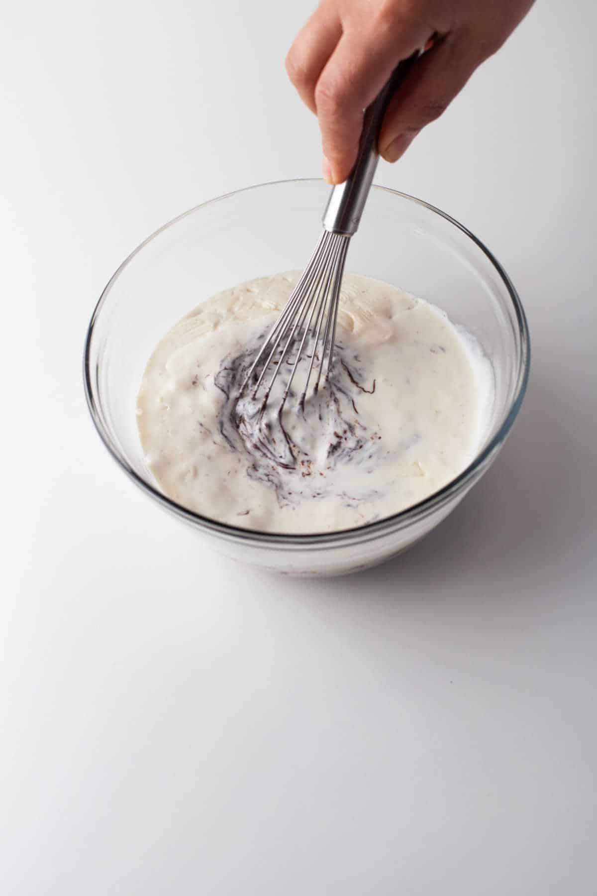 A whisk stirring hot cream and chocolate chips together. 