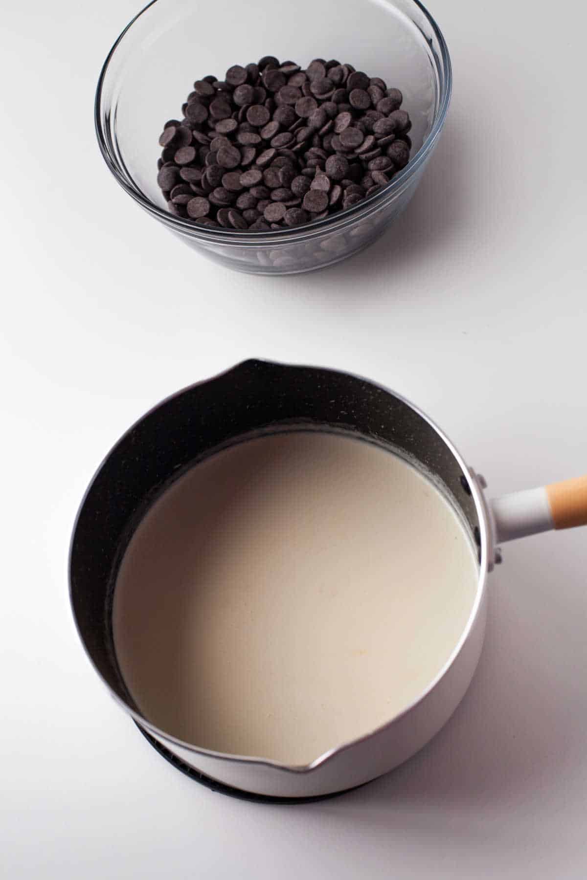 Chocolate chips in a glass mixing bowl and cream in a saucepan. 