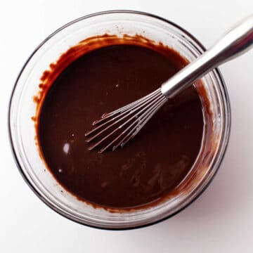 Chocolate ganache with a whisk in it in a glass mixing bowl.
