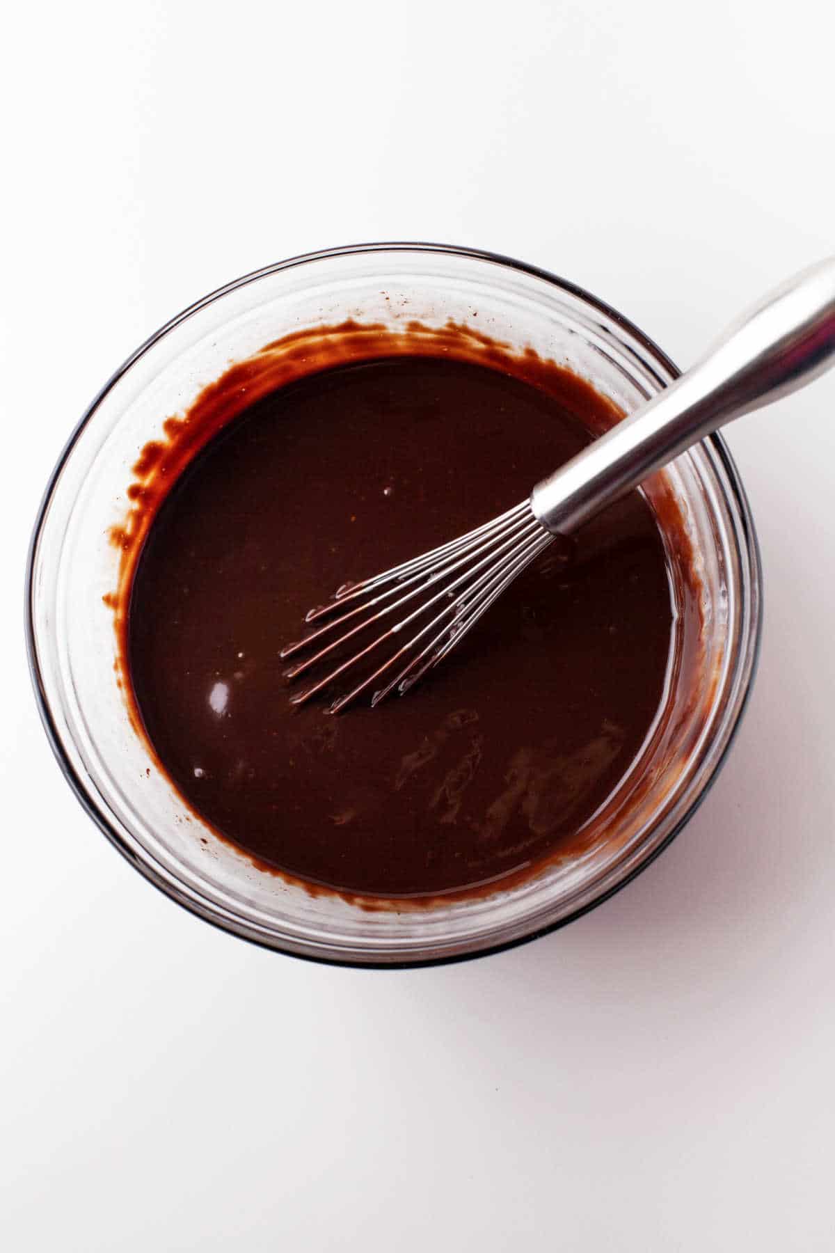 Chocolate ganache with a whisk in it in a glass mixing bowl.