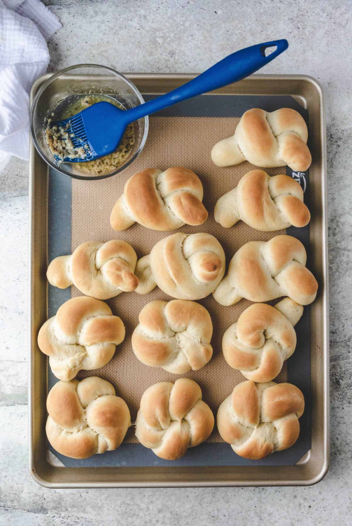 Baked garlic knots on a tray next to a dish of garlic butter.