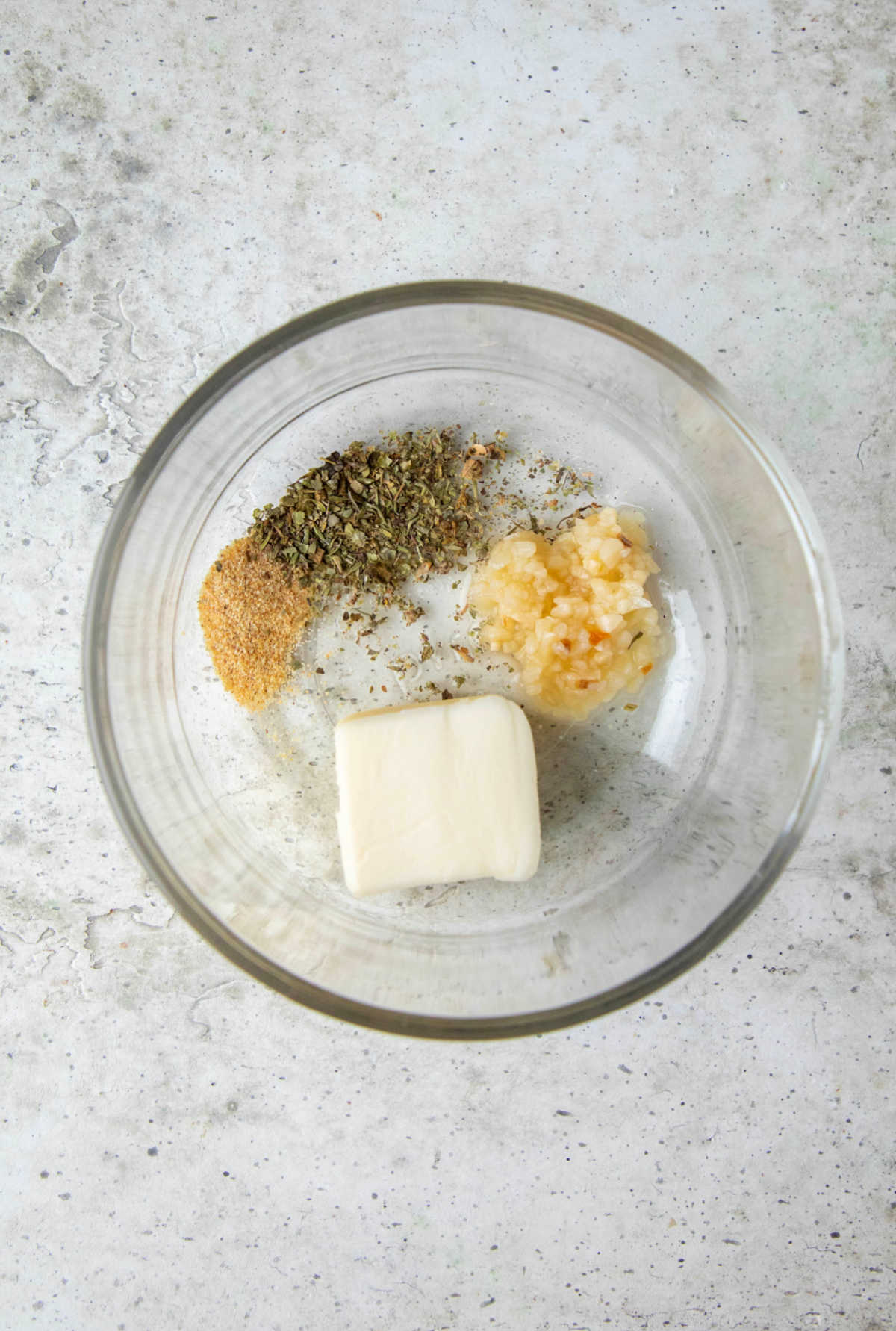 Ingredients for garlic butter in a glass mixing bowl. 