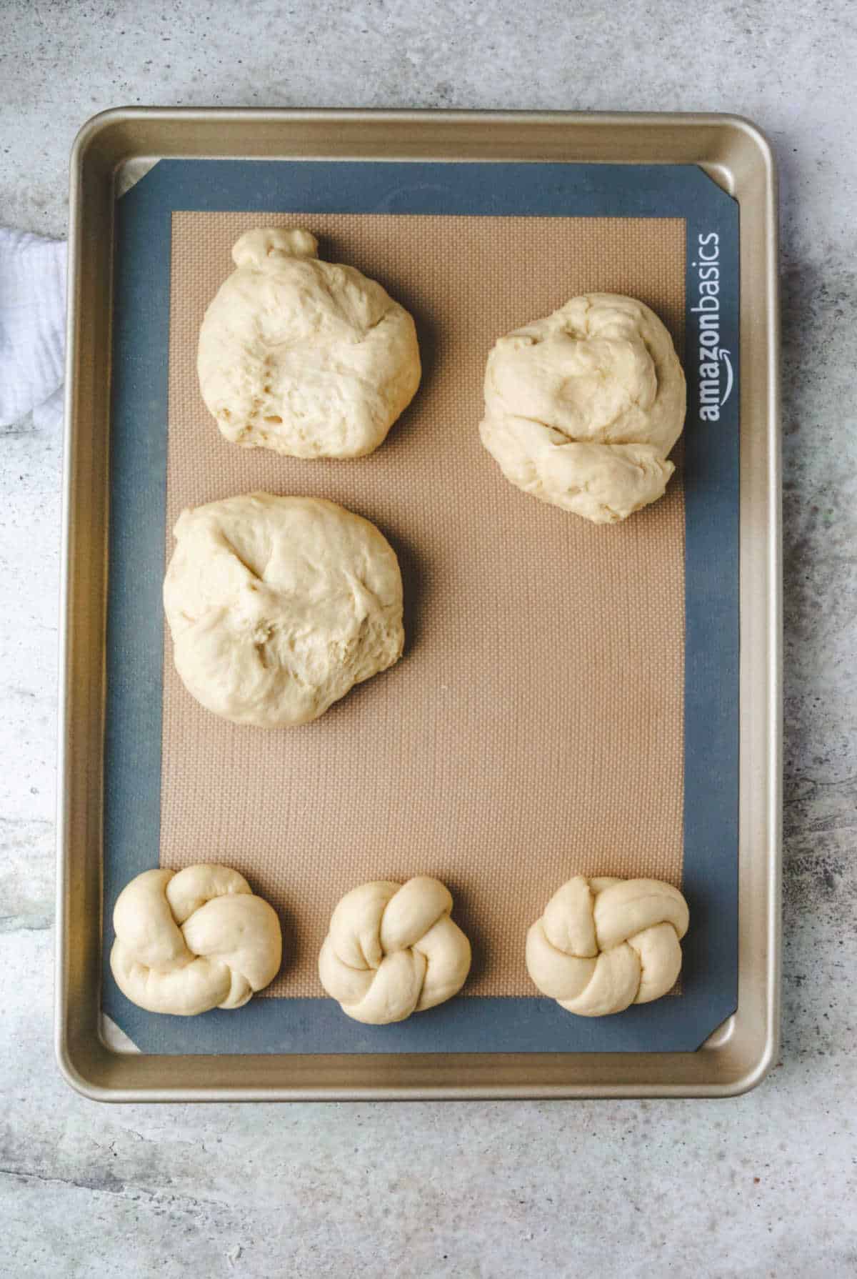Pieces of dough being shaped into knots on a baking sheet. 