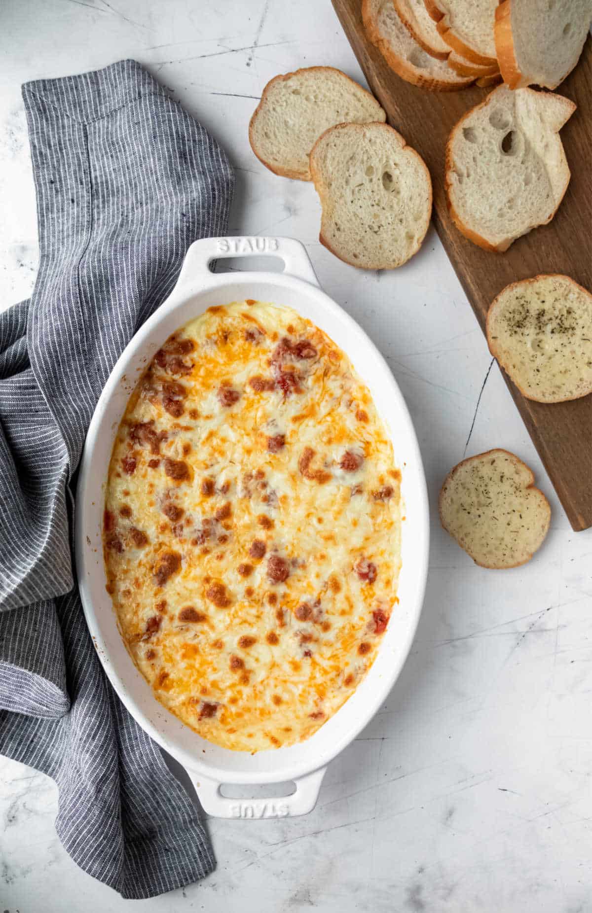 A white dish of lasagna dip surrounded by baguette slices. 