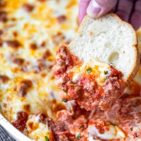 A toasted baguette slice scooping up lasagna dip.