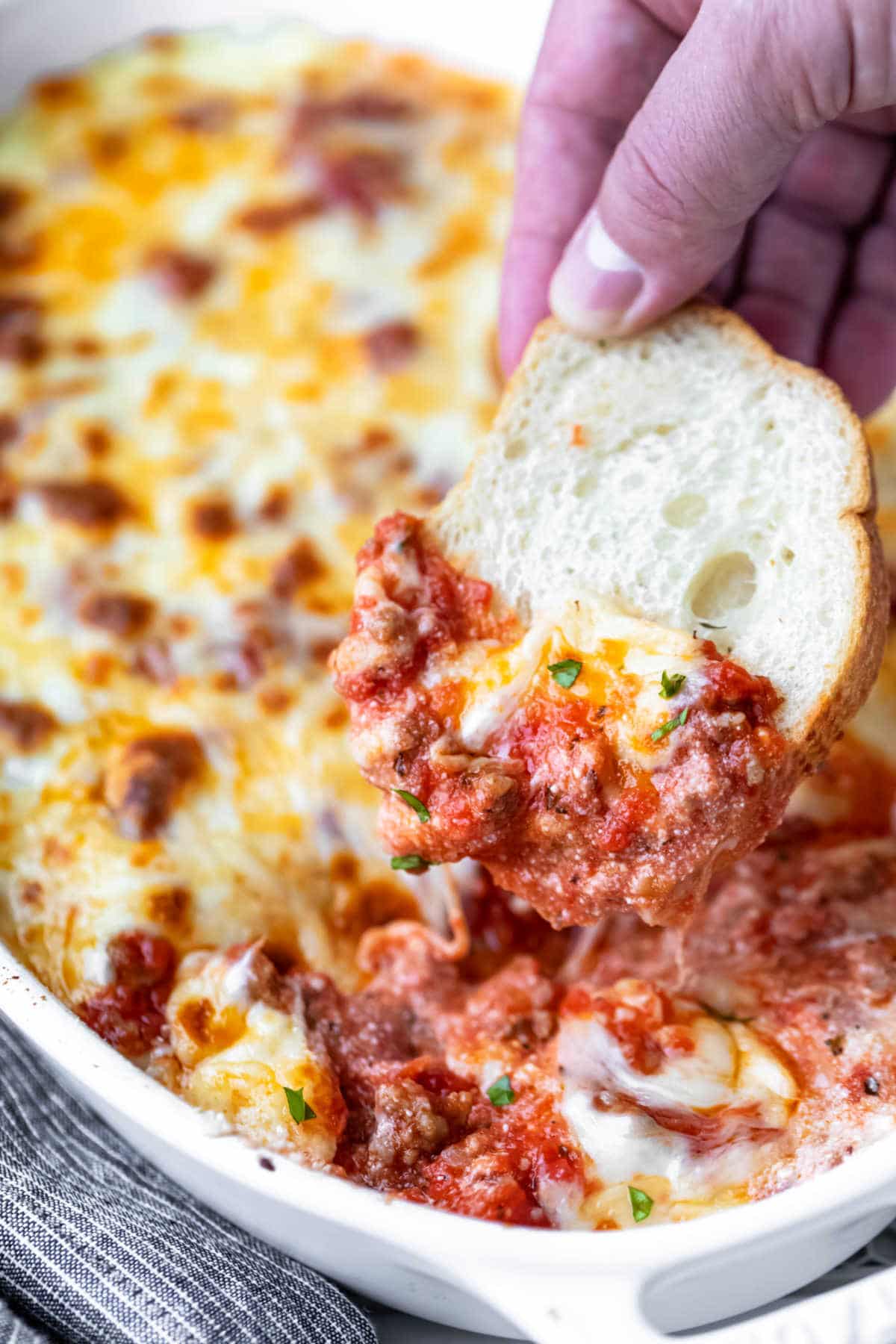 A toasted baguette slice scooping up lasagna dip.