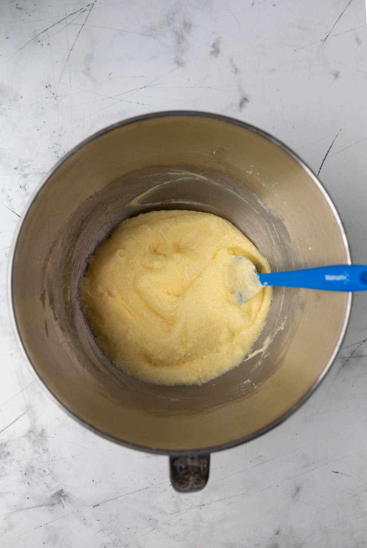 Eggs mixed into creamed butter and sugar in a silver mixing bowl. 