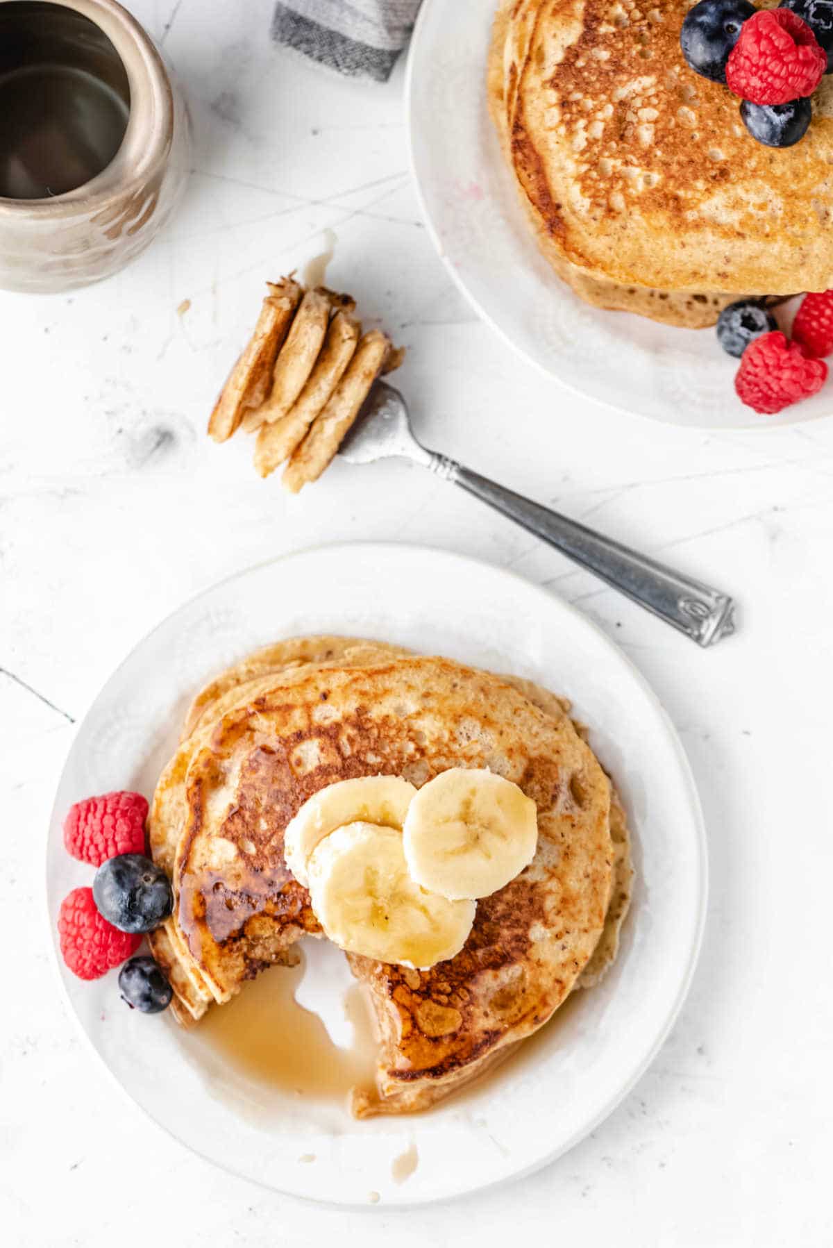 A stack of whole wheat pancakes with banana slices and berries next to it. 