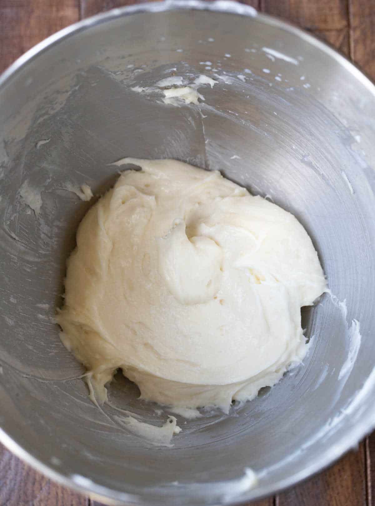 Cream cheese and sugar in a silver mixing bowl. 
