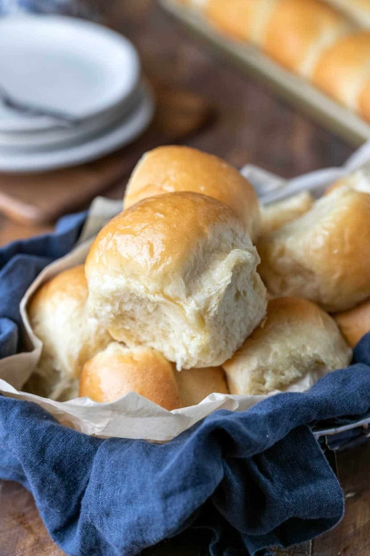 A basket of homemade dinner rolls next to a stack of plates. 