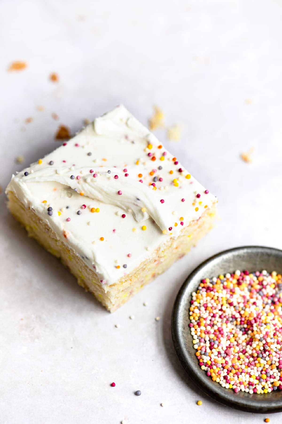 A slice of funfetti cake next to a dish of sprinkles. 