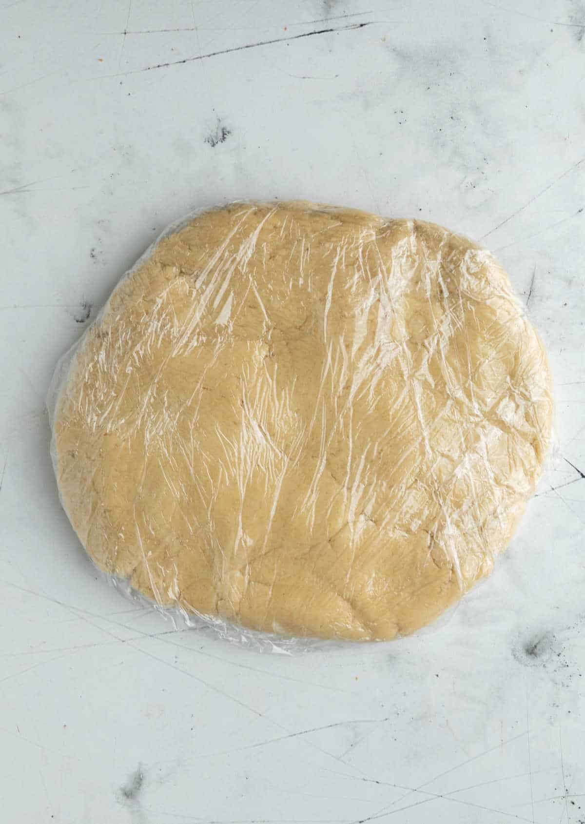 Sugar cookie dough disk wrapped in plastic wrap. 