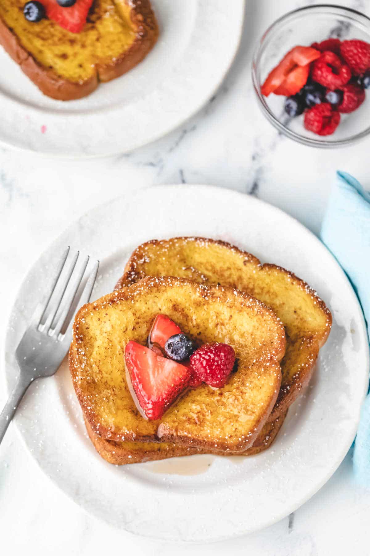 A plate of brioche french toast next to a bowl of berries. 