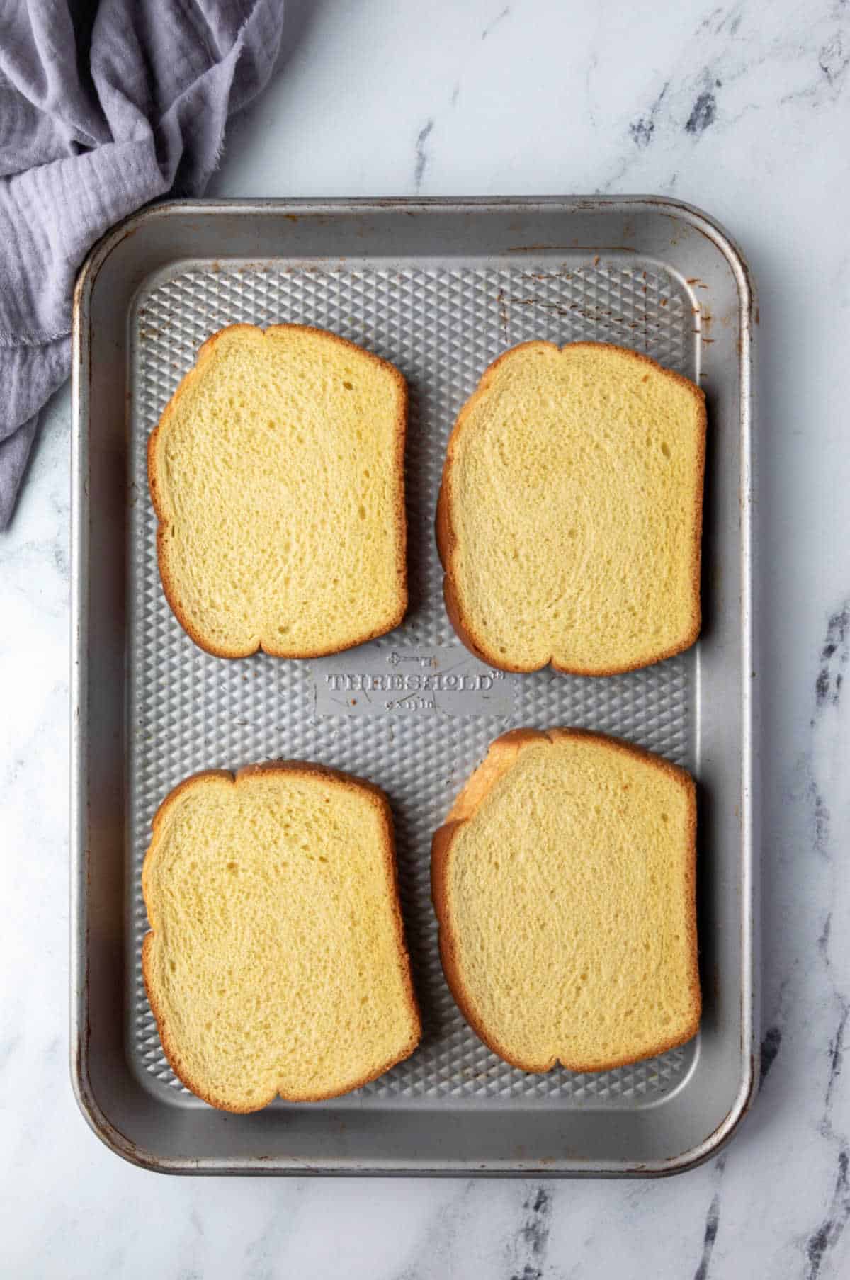 Four slices of brioche on a baking sheet.