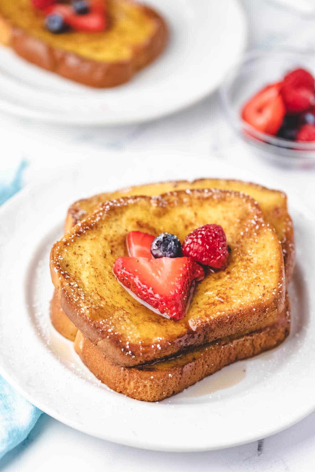 Three slices of brioche french toast covered with syrup and berries.