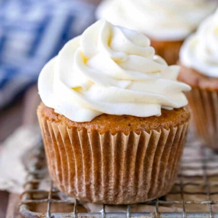 Cupcake with cream cheese frosting on a wooden cutting board.