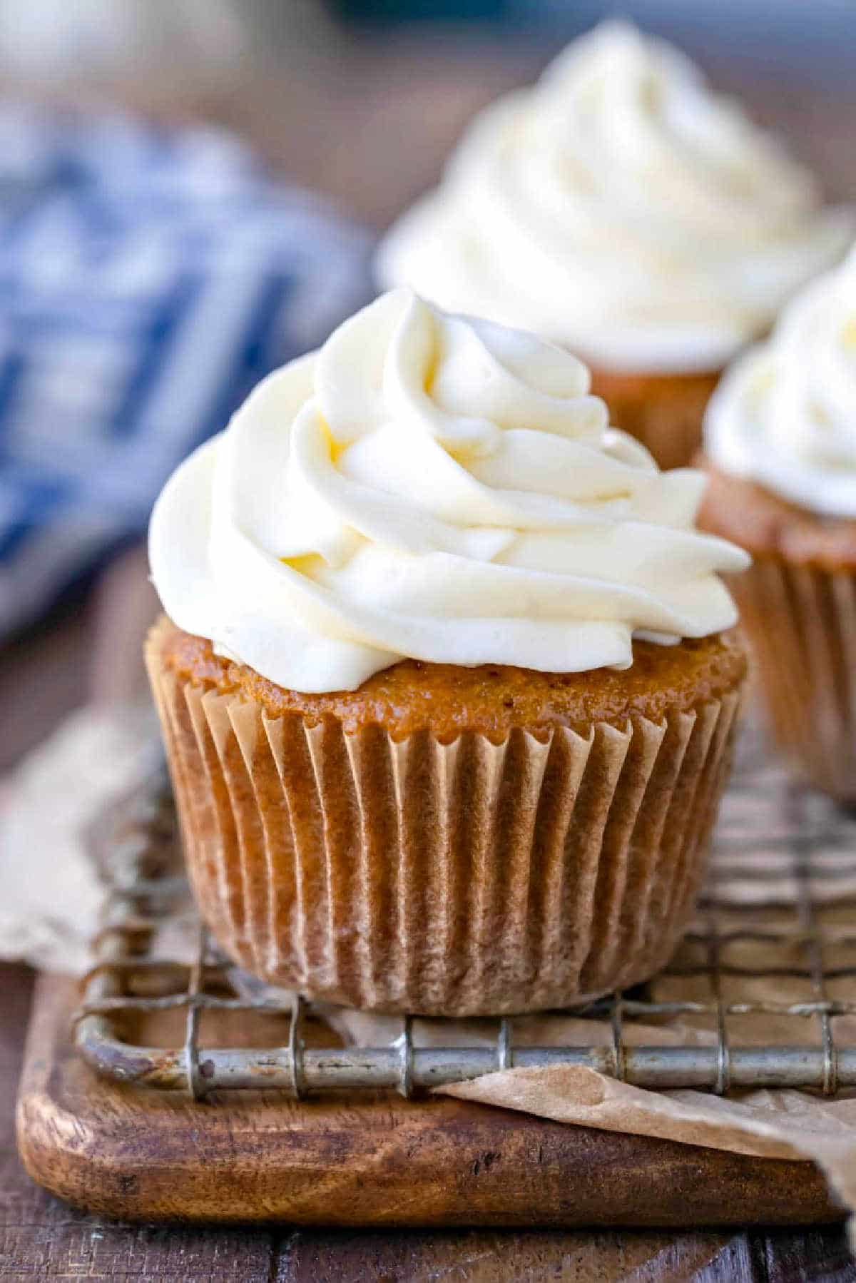 Cupcake with cream cheese frosting on a wooden cutting board. 