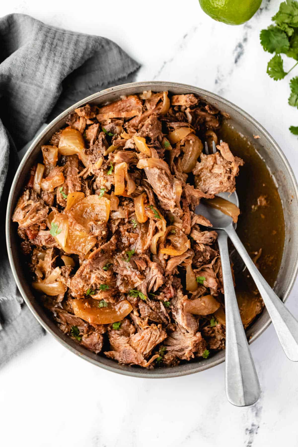 Overhead view of a dish of Mexican shredded beef next to fresh cilantro. 