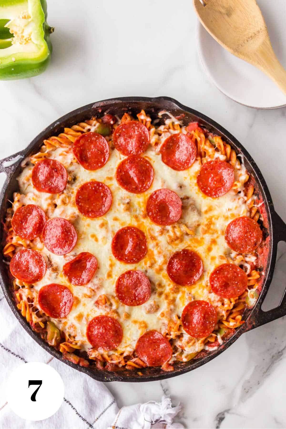 Pizza pasta in a pan next to a wooden spoon.