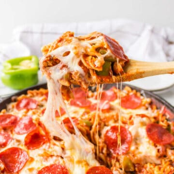 A wooden spoon lifting a scoop of pizza pasta from a skillet.