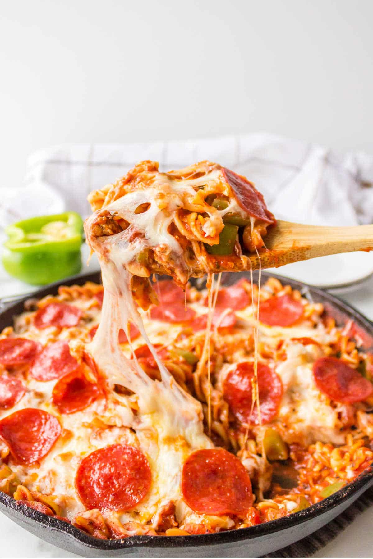 A wooden spoon lifting a scoop of pizza pasta from a skillet.