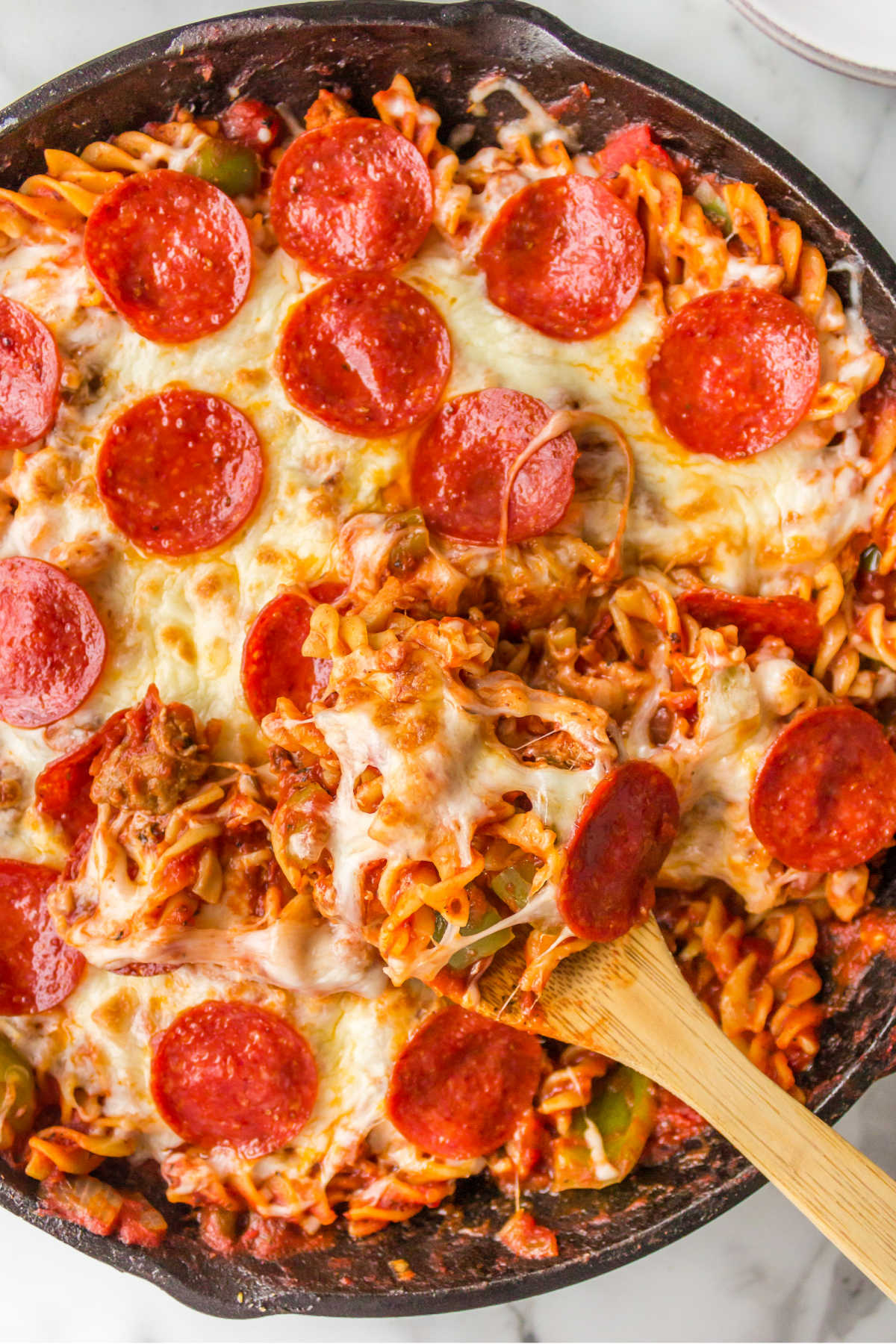 A wooden spoon in a pan of pizza pasta. 